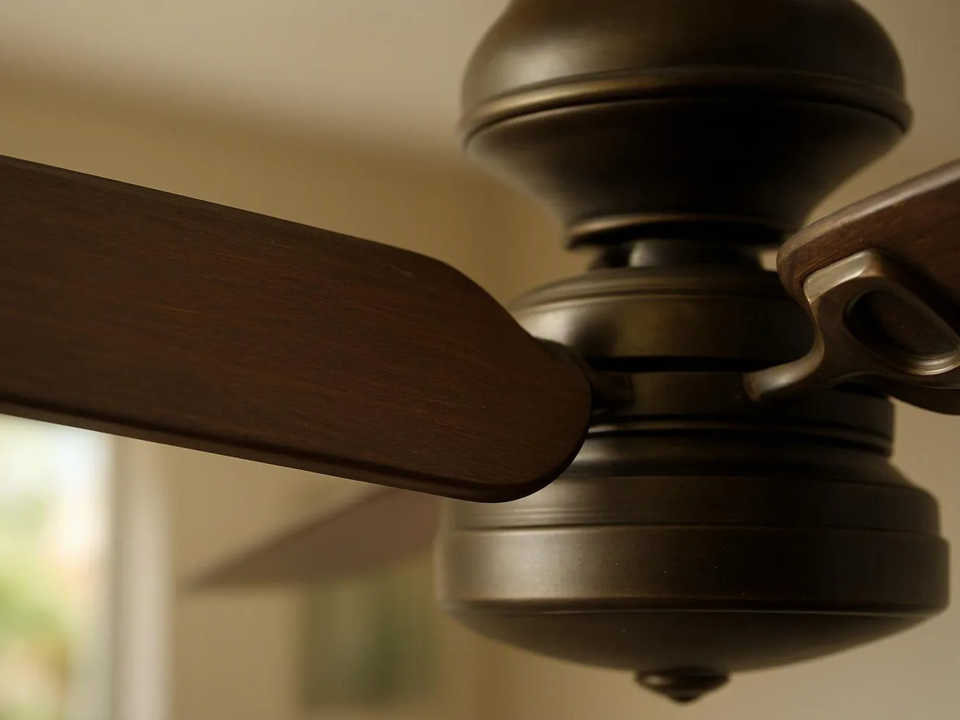 Close-up of a dark ceiling fan with wooden blades against a soft beige indoor background