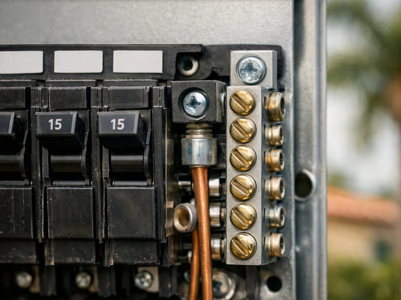 Close-up of an electrical breaker panel with numbered switches, copper wiring, and brass terminal screws inside a metal box