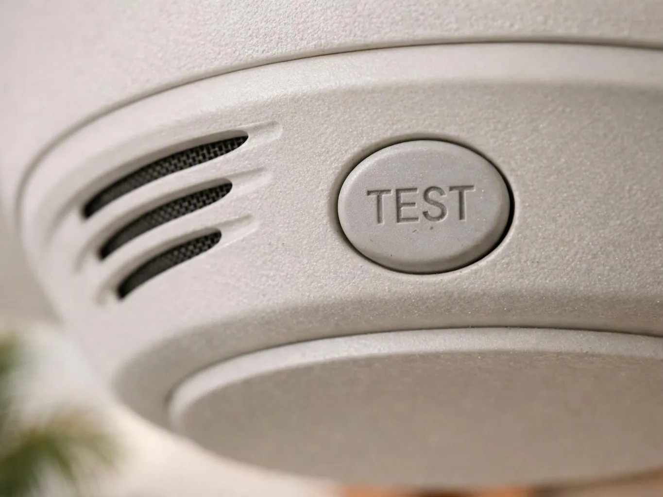 Close-up of a white smoke detector with a TEST button and vent slits on the ceiling